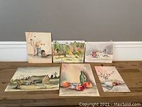 Group photo showing all six watercolor paintings positioned on a wooden floor against a gray wall.