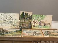 Six watercolor paintings placed on a table showing various Canadian landscape and rural scenes.