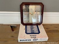 Full view of Bulova wall clock displayed on its original quartz clock box and desk clock beside it on the table