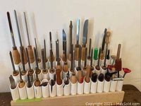Full view of PVC tube rack holding approximately 30 assorted awls and poking tools