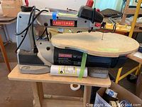 Front view of the Craftsman scroll saw on a wooden rolling cart showing the saw blade, wooden work table, and motor base.