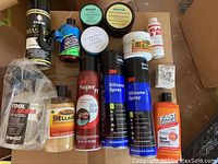 Lot overview of assorted cleaners, conditioners, polishes, glues in varied packaging arranged on floor.