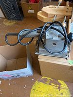 Milwaukee orbital sander on cardboard box, cord wrapped over sander, background shows work area.