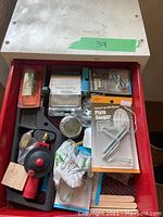 Top drawer open showing plate hanger package, wire brush wheel, suction pump tool, wooden stir sticks and assorted small fasteners
