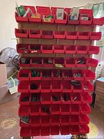Front view of the hardware cart showing multiple rows of red compartments filled with assorted hardware items such as screws, nails, and other small parts.