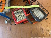 Photo showing two utility work lights, one black Craftsman brand and one red, both with protective cages, on the floor near the cart.