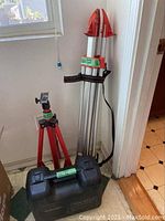 Two tripods leaning against wall next to carrying case and strap