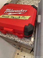 Red Milwaukee hard case labeled as containing round drill bits, placed on a granite countertop.