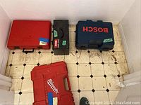 Overview of four closed carrying cases on tile floor: red case, black case, blue Bosch case, red Milwaukee case