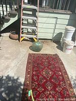 Overview of rug, glass bottle, and ladder on exterior concrete