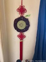 Jade circular wall hanging with red decorative tassels against white wall