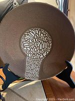 Brown ceramic decorative plate with abstract white pattern on a stand