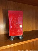 Red rectangular plaque on small metal stand displayed on wood shelf