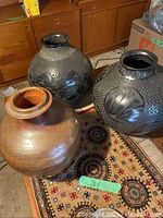 Three vases grouped on patterned rug, two blackware and one brown