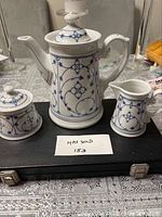 3-piece Schonwald coffee set on black case; white porcelain with blue floral and geometric pattern, includes coffee pot, sugar bowl with lid, and creamer.