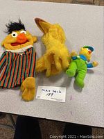 Three Sesame Street puppets including Bert hand puppet, Big Bird plush puppet, Ernie plush with small Bert toy, arranged on table