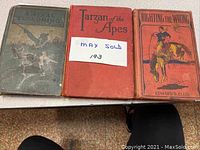 Three vintage books displayed side by side on a table: A Final Reckoning, Tarzan of the Apes, Righting the Wrong.