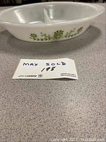 Side angled view showing the oval shape, white opaque glass, and green floral pattern on the exterior.