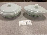 Two white oval covered casserole dishes with green floral pattern on sides, placed on a table with MaxSold lot label.
