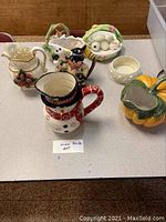 Overview of six ceramic holiday-themed pitchers and bowls displayed on table.