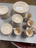 Photo showing the full collection of Pfaltzgraff dinnerware including stacked dinner plates, salad plates, bread plates, bowls, and several mugs arranged on a table.