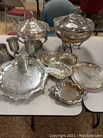 Full display of lot with all serving pieces arranged on table including chafing dishes, trays, pewter goblets, and divided dish.