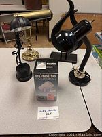 Photo showing four lamps and an abstract black circular sculpture on a table with cords visible.