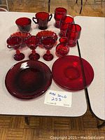 Front view of red glass plates, goblets, cups, tumblers and small dishes arranged on a table.