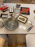 Table displaying a variety of vintage metalware, toys, games, and collectible items arranged for lot description.
