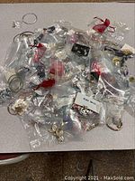 Wide view of a large assortment of individually bagged jewelry items including earrings, rings, bracelets, and pendants on a flat surface.