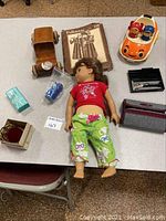 Lot displayed on a table showing the American Girl doll, Mattel toy car, wooden toy car, sewing pattern, small boxed items and accessories