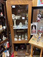 Full view of wood single door curio cabinet with glass front filled with ceramic items.