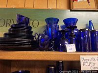 Full view of stacked blue plates alongside blue glassware and two vases on shelf