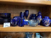 Blue glass dishes, bowls, cups, small bottle, clear glass bowl, and two Chinese-style blue ceramic vases with floral/gold decorations on wood shelf.