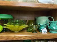 Shelf with assorted green glassware including vases, a pitcher, dishes, and a candy dish.