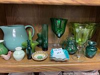 Shelf with assorted green glassware, ceramic pitcher, trinkets including a small green bird figurine, small plates and decorative dishes