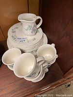 Dinnerware set stacked showing plates, cake plates, cups, and pourer with grapevine pattern.