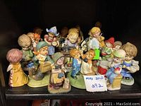 Photo showing the full set of 17 ceramic figurines styled to resemble Hummel figurines on display shelf.