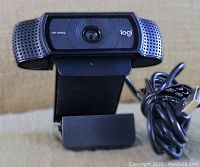 Front view of Logitech Pro Stream Webcam showing lens, logo, and mounting clip with USB cable coiled beside it.