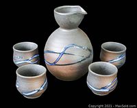Photo showing the ceramic sake bottle and four matching cups with beige and brown coloring and blue wave decoration.