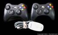 Two black Xbox 360 wireless controllers shown with white Microsoft wireless receiver and USB cable coiled beside them.