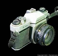 Front-side angle view of Pentax K1000 with attached 50mm lens, showing model and Pentax branding, strap mounted.