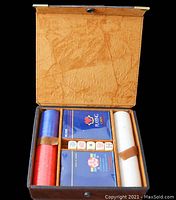 Open brown leather poker case containing three stacks of red, white, and blue poker chips, two sealed decks of playing cards, and five dice.