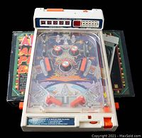 Front view of the Tomy Atomic Arcade tabletop pinball game on top of its original box. Shows plastic white body with colorful playfield under transparent cover, scoring units at the top.