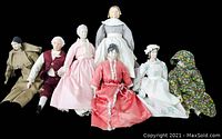 Seven colonial porcelain dolls displayed together showcasing varied period outfits and styles