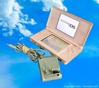 Nintendo DS Lite coral pink open showing the Nintendo DS boot screen with charger cable beside it