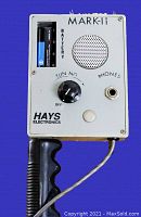 Close-up of the MARK-II control box showing tuning knob, speaker, phone jack, and battery compartment missing the cover, attached to black handle with cable.