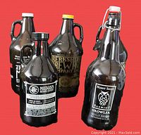 Five amber glass growlers with distinct brewery logos and artistic labels, shown against red background.