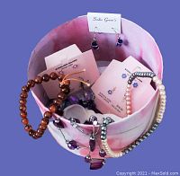 Pink round trinket box with bracelets, earrings on cards, and necklaces inside