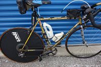Full side view of gold Colnago road bicycle showing frame, saddle, handlebars, water bottles, packs and wheels